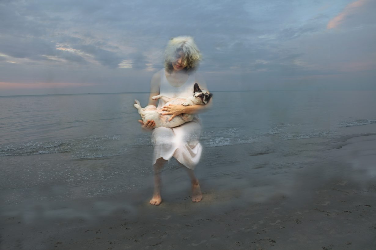ビーチでパグを抱きかかえる女性を写した、ぼやけたイメージ 