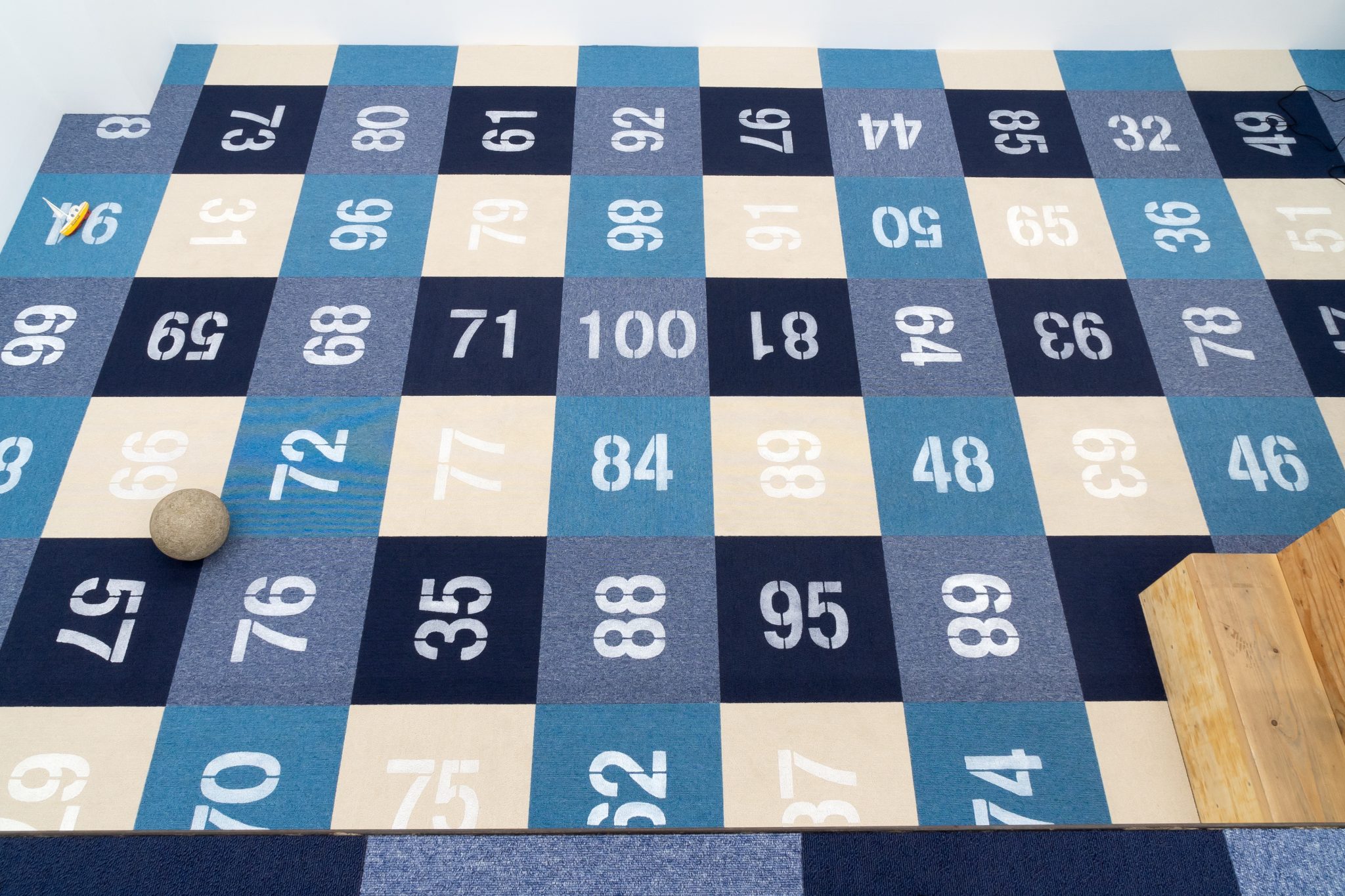 gallery floor covered with a grid of checkered carpet samples stenciled with numbers