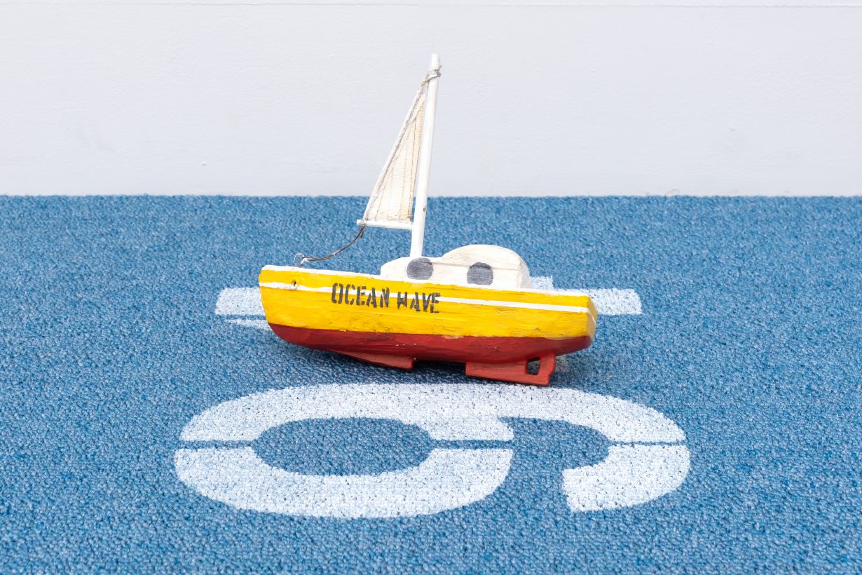 数字の94がプリントされたカーペットに置かれた、「OCEAN WAVE」と書かれたおもちゃの船。