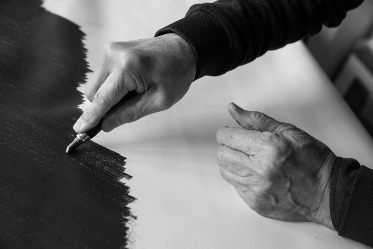 a close-up photograph of the artist Takesada Matsutani's hands applying graphite on paper