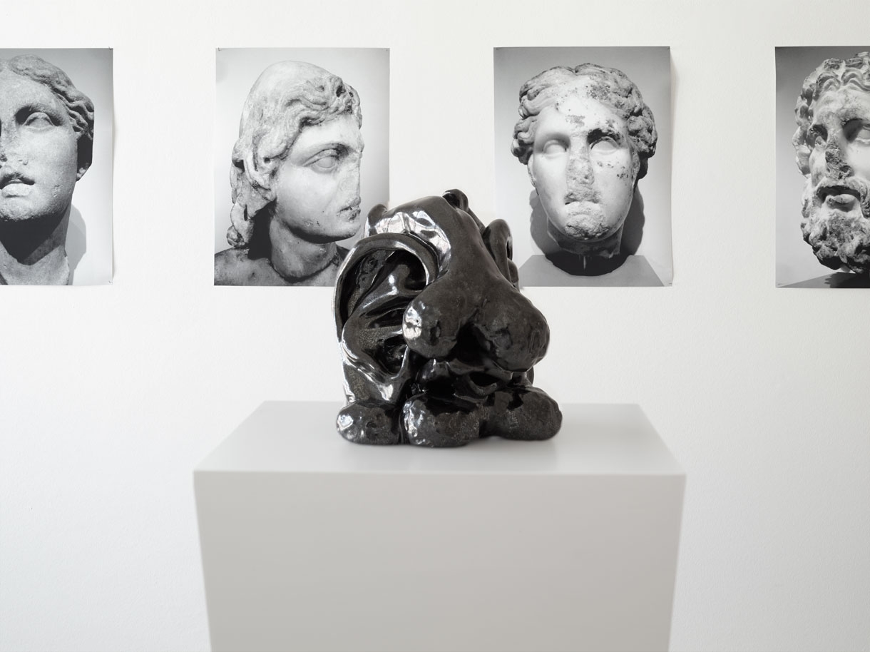 Blake’s Paranoia, 2013, ceramic on pedestal, 24 × 16 × 16 cm (foreground) and Heads, 2013, prints, 46 × 34 cm (background). Photo: Simon Vogel. Courtesy the artist & Lars Friedrich, Berlin