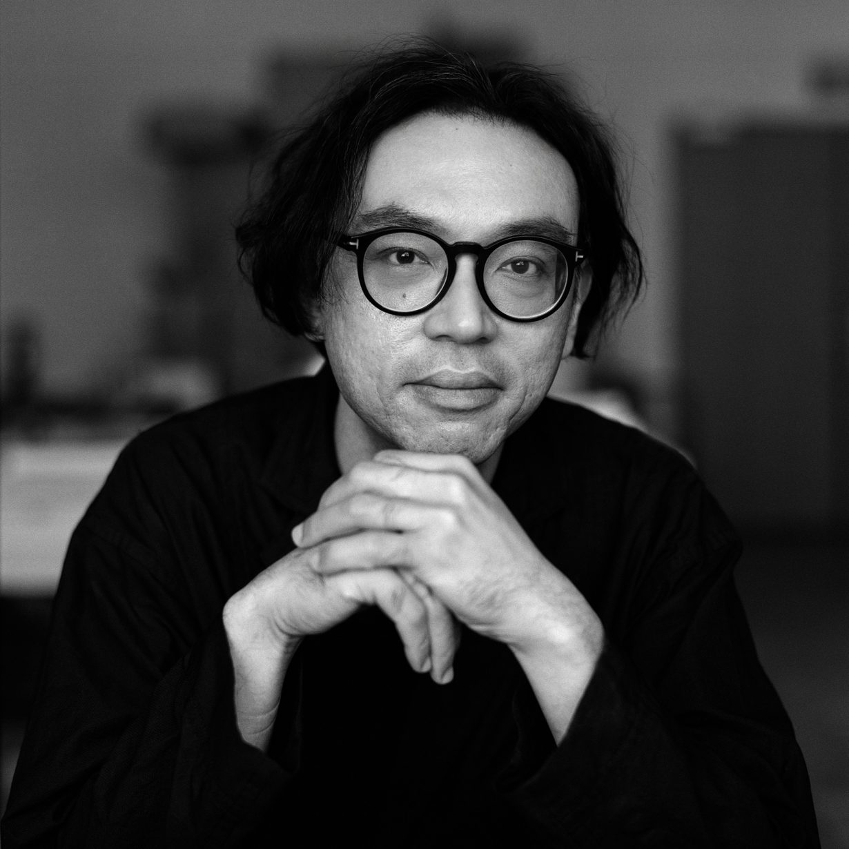 Black and white portrait of Ho Tzu Nyen. He is dressed in black, wearing glasses.