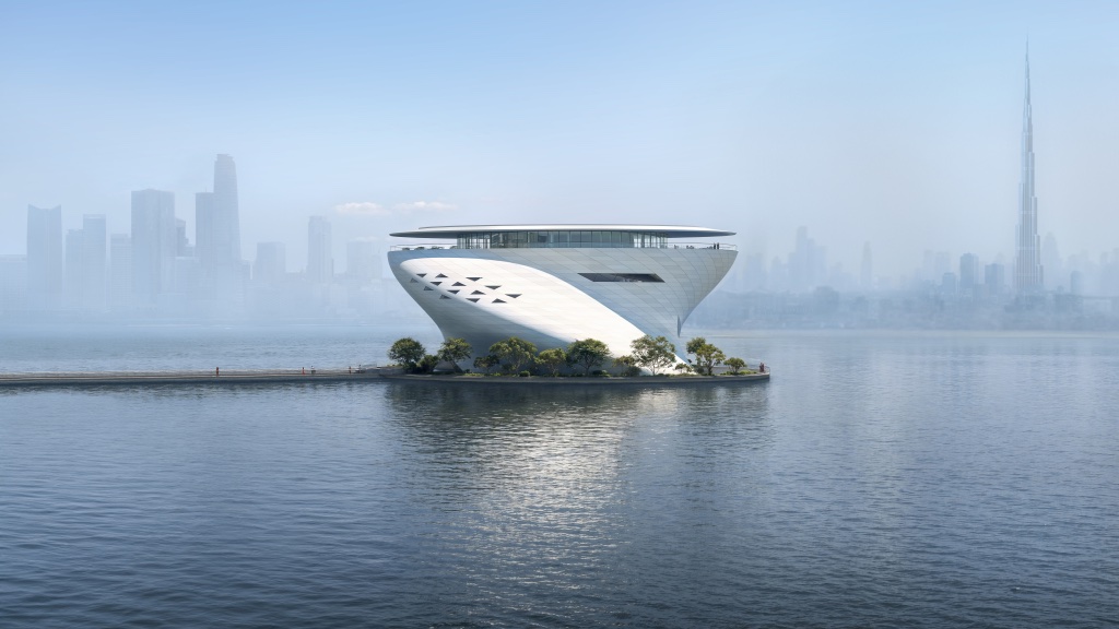 A render of the Dubai Museum of Art seen from the side. It is on a jetty in the middle of a body of water and set against the Dubai skyline.
