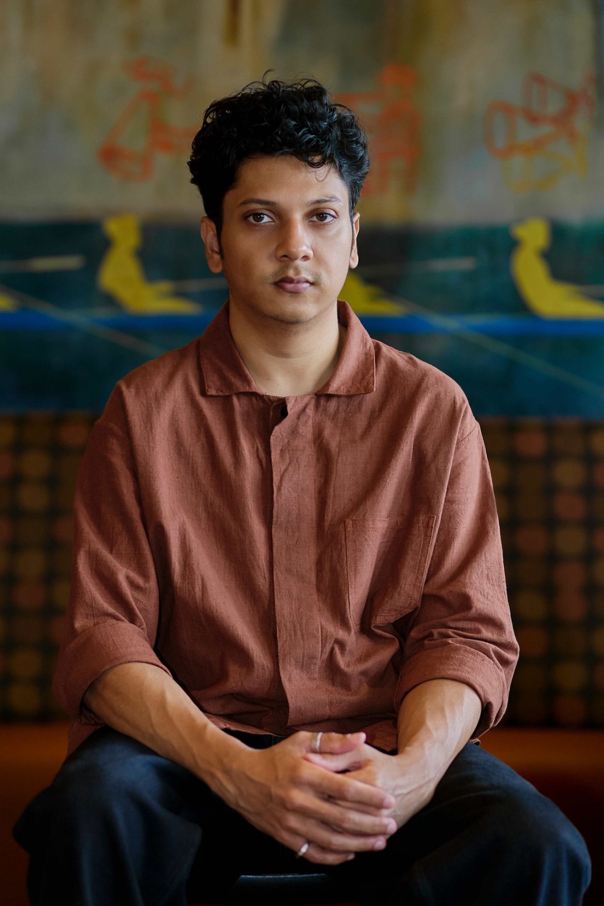 Vishal Kumaraswamy sitting facing the viewer in front of a blurred colourful background