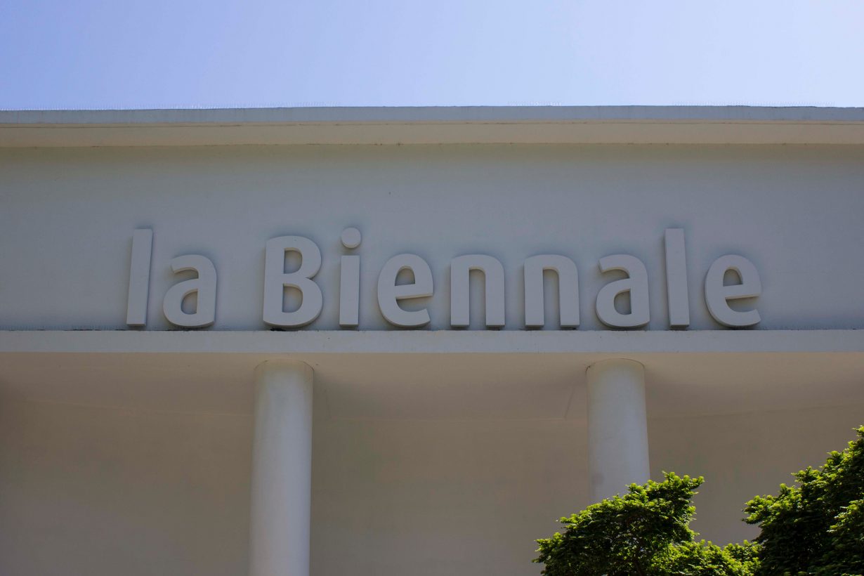 A closeup of the front of a white building with the words La Biennale inscribed in relief on the frieze