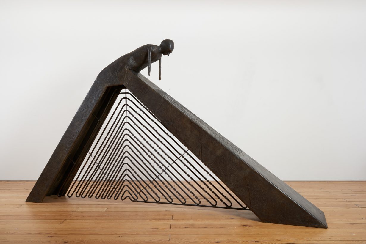 A sculpture made of a dark material and resembling a bent-over body