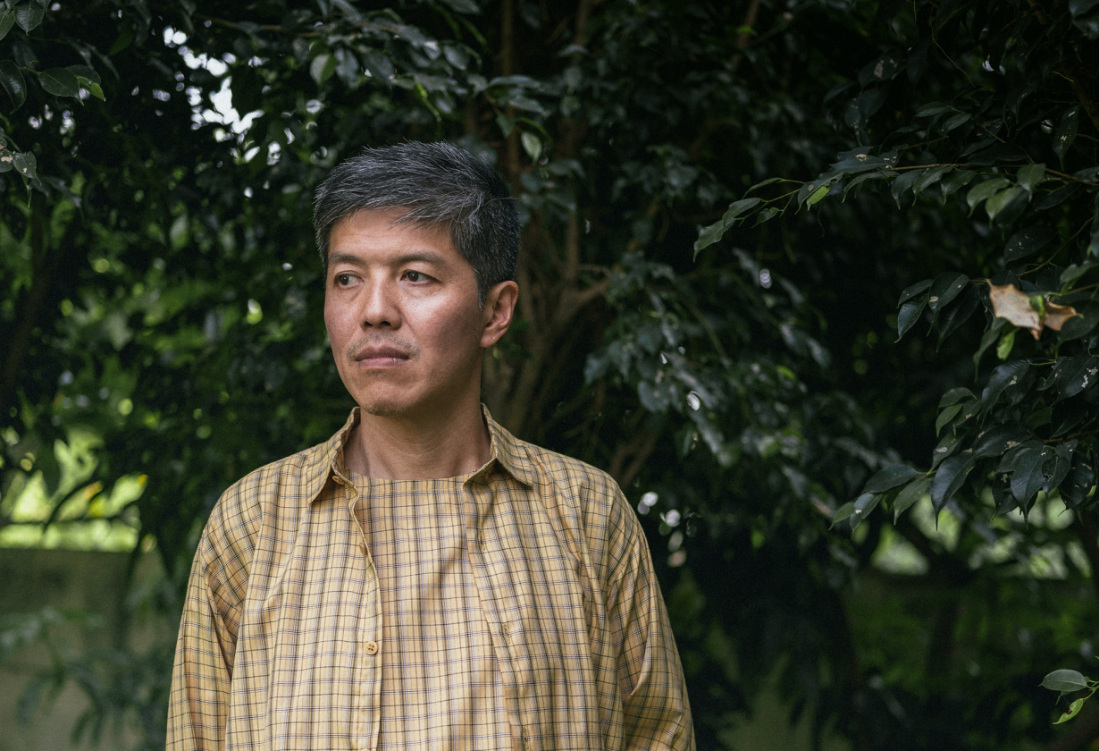 Portrait of John Tain in a checkered shirt in front of a tree