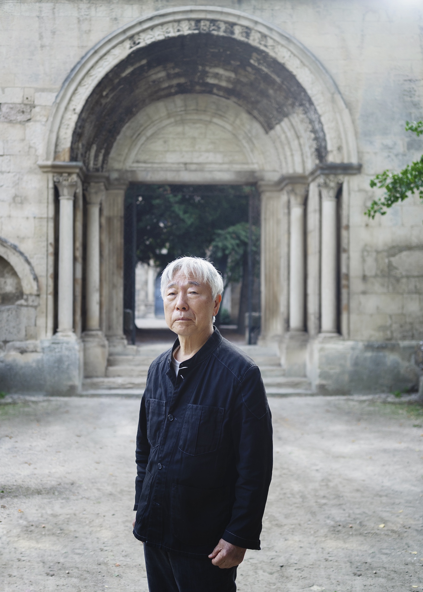 Lee Ufan dressed in black standing in front of a stone archway