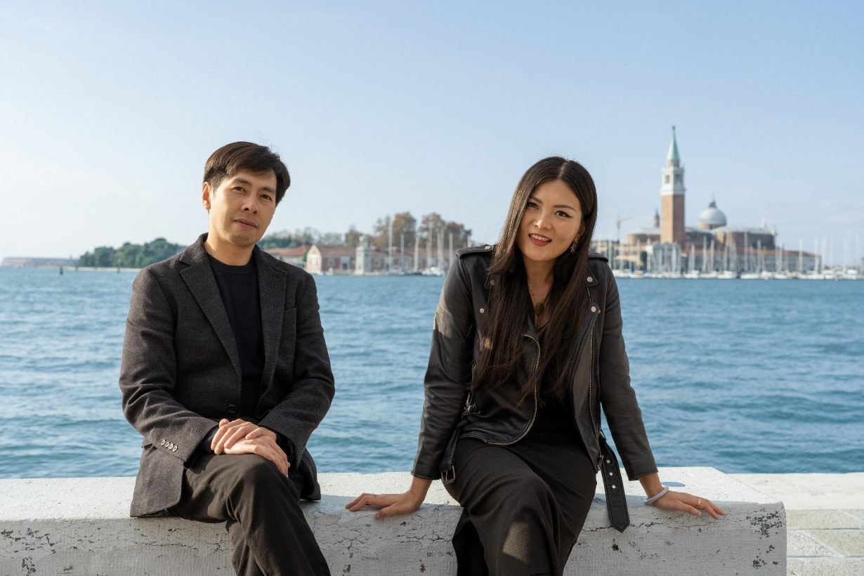 Artists Kingsley Ng and Angel Hui sit in front of a view of Venice