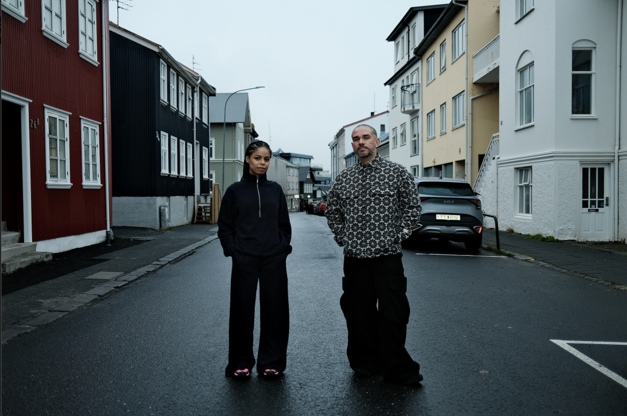 Photo shows Raphael Fonseca and Yina Jiménez Suriel standing in a street of coloured houses in Reykjavik. The sky is grey.  