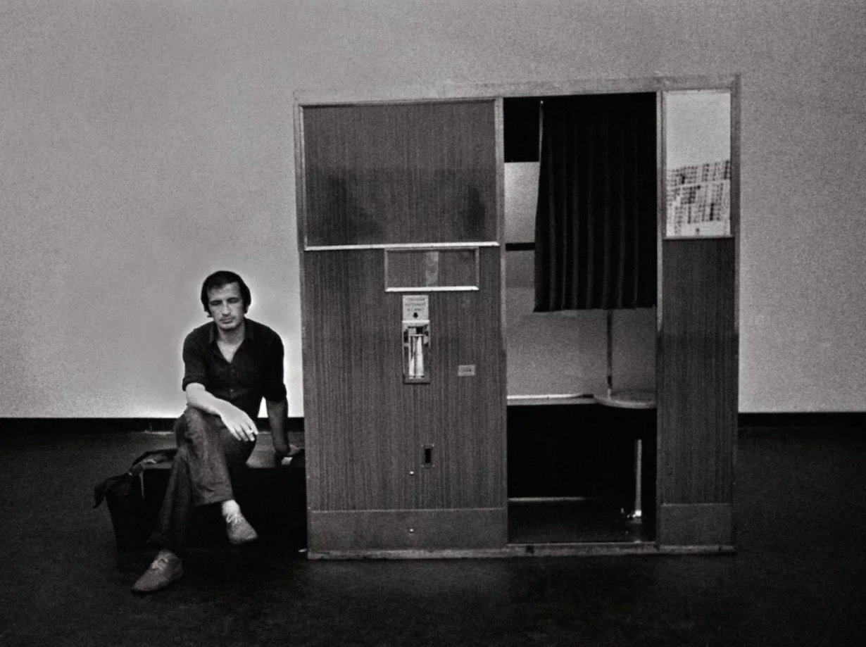Black and white photograph of Franco Vaccari sitting next to a photo machine