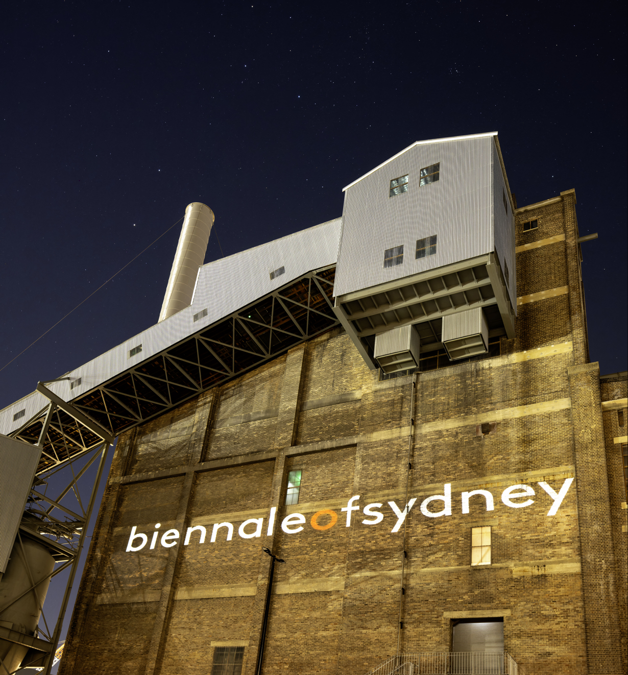 A brick building seen at night with the words 'biennale of sydney' painted on its facade