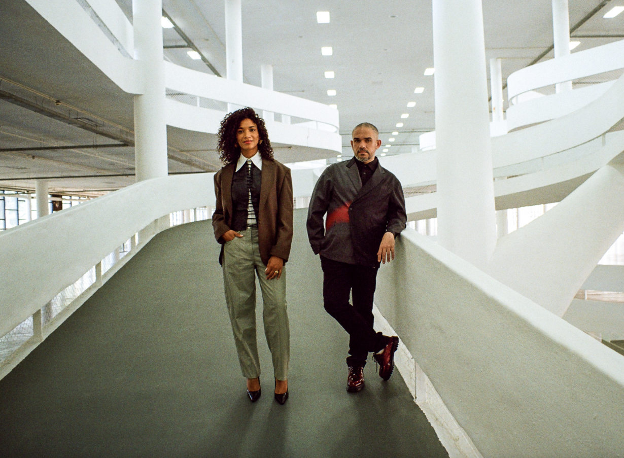 Portrait of Amanda Carneiro and Raphael Fonseca. standing at the bottom of the sweeping internal ramp of the modernist Bienal Pavilion 