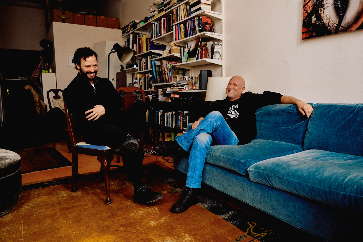 Eli Scheinman and Trevor Paglen sitting together and laughing in a living room