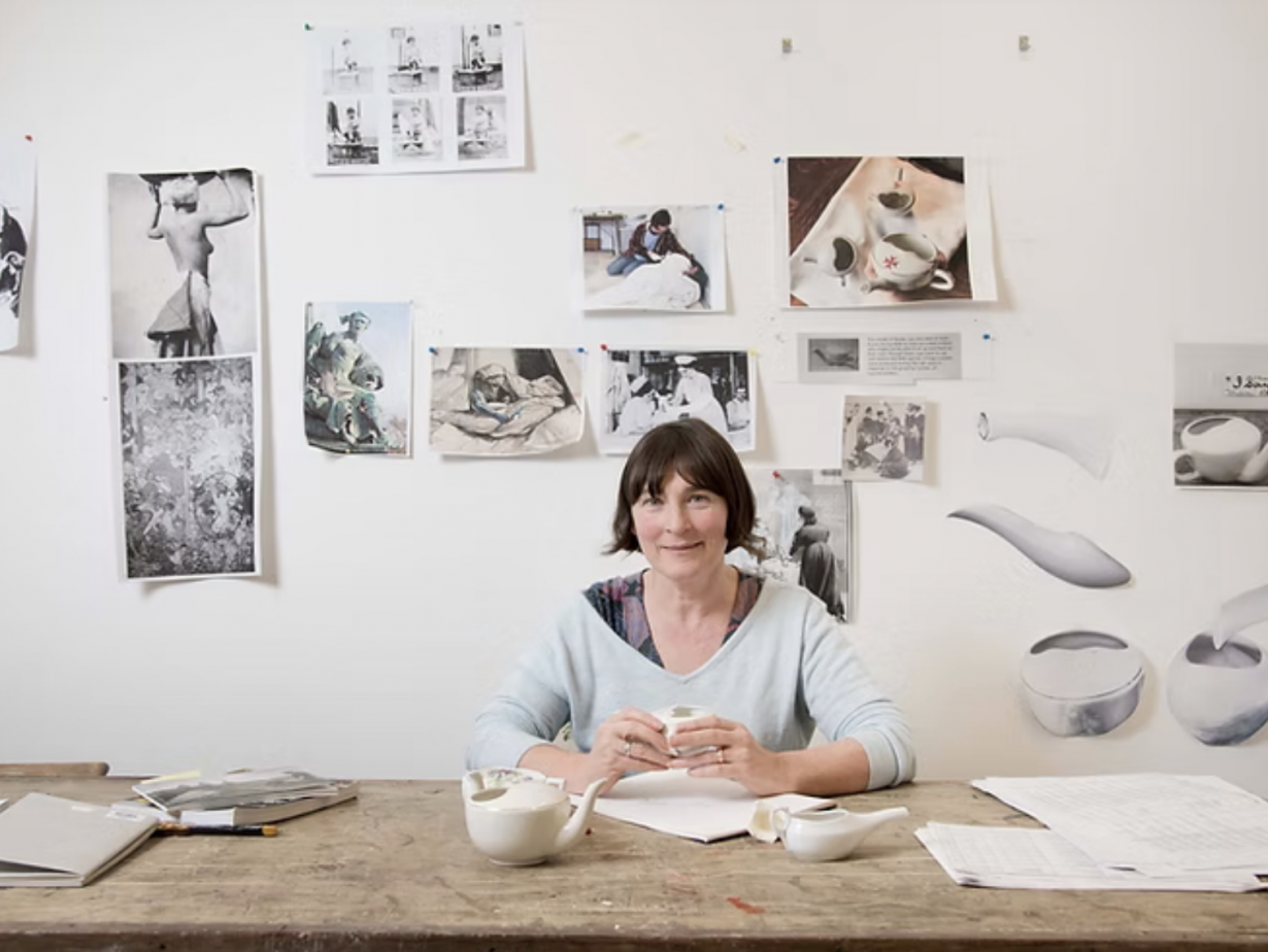 Christine Borland, sat at a table in her studio, various reference material stuck to the wall behind