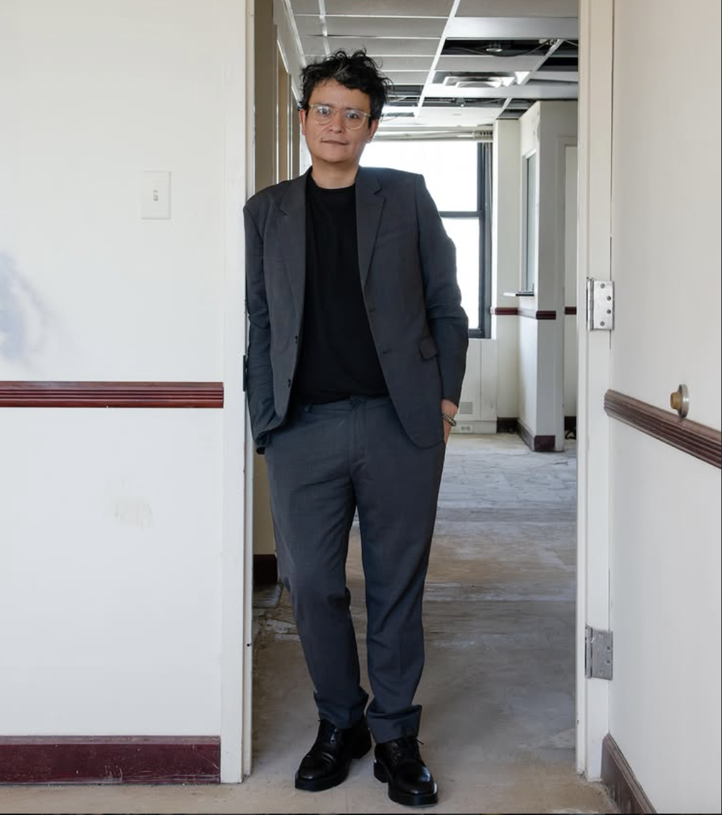 Portrait of Francisco Correa Cordero standing. Her wears glasses, a black t-short and grey suit