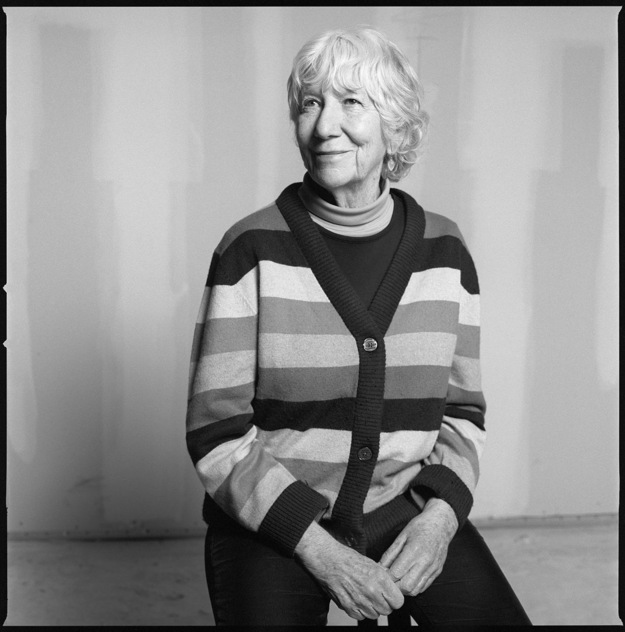 black and white photo of Mary Heilmann, sat in a striped cardigan