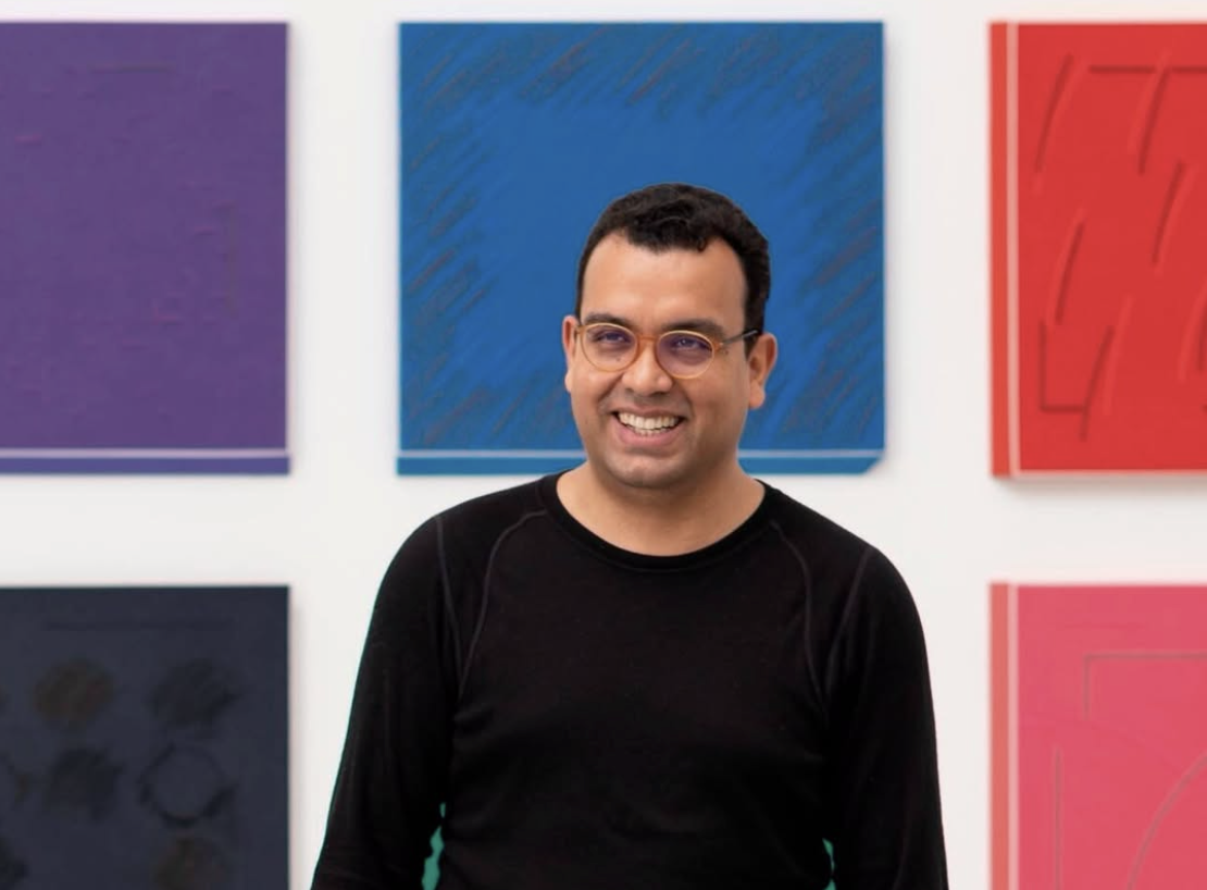 Rodrigo Cass stands in front of a grid hang of monochrome canvases